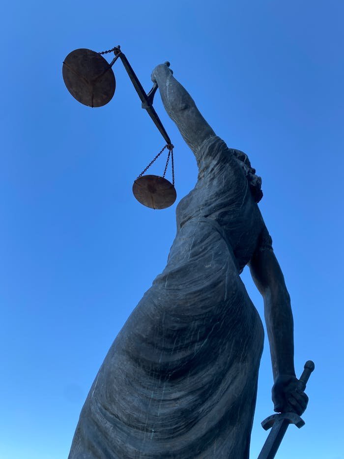 Majestic bronze statue holding a sword and scales representing justice against a clear blue sky.